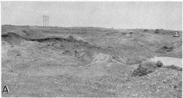 Black and white photo of quarry; gentle hills with little relief; front-end loader in background.