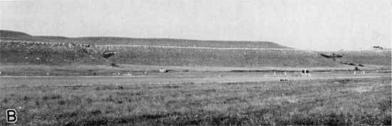 Grass-covered hill above plain; prominent limestone bed three-fourths of the way up on the hillside.